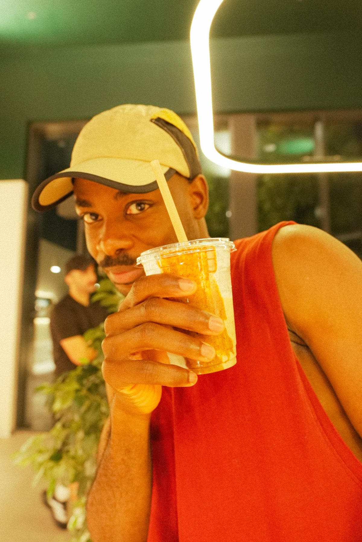 A runner in a cap raising an iced drink to the camera after the Backyard run