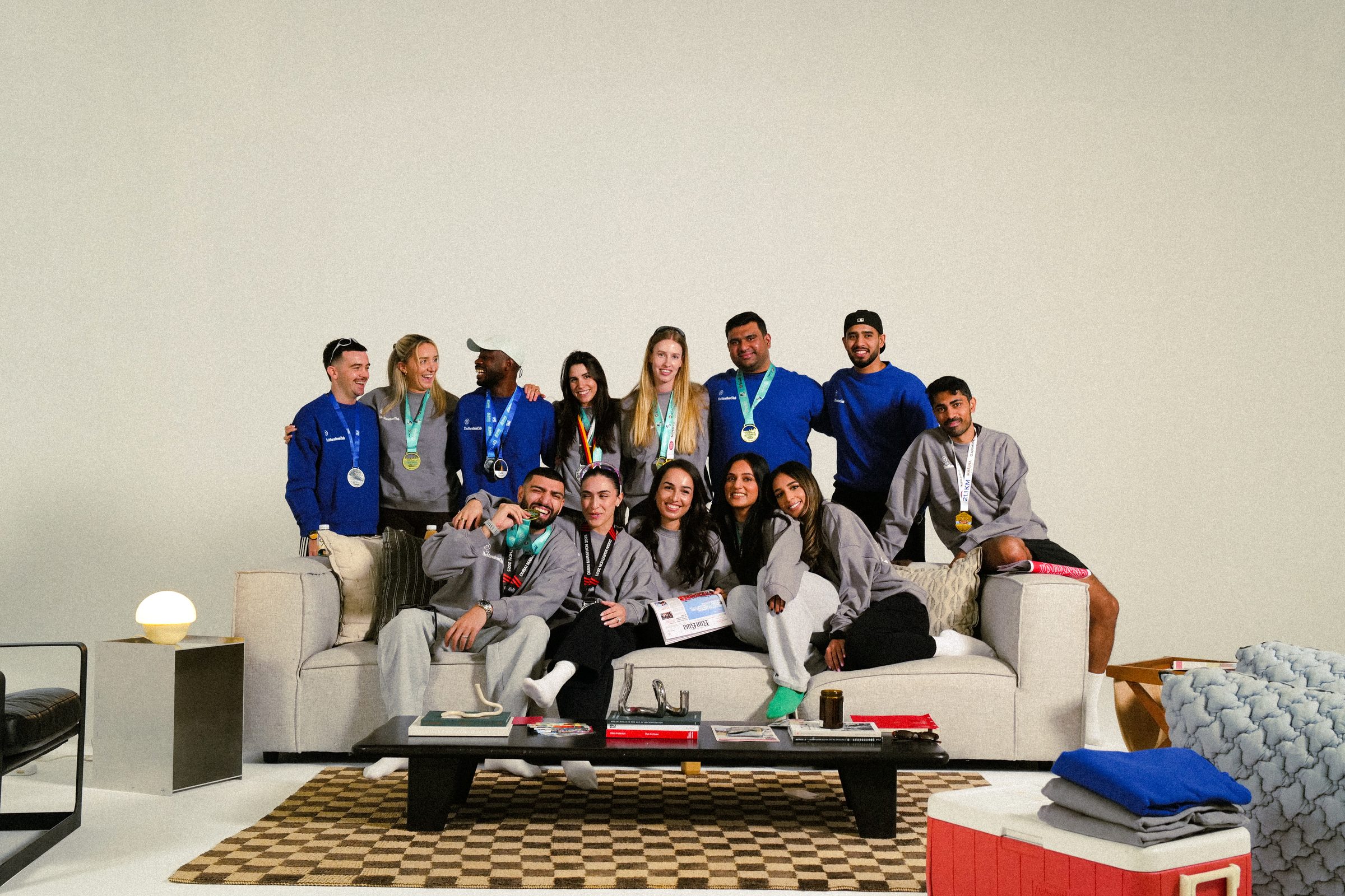 TheMarathonClub members on a sofa in the studio, in blue and grey club crewnecks with their race medals