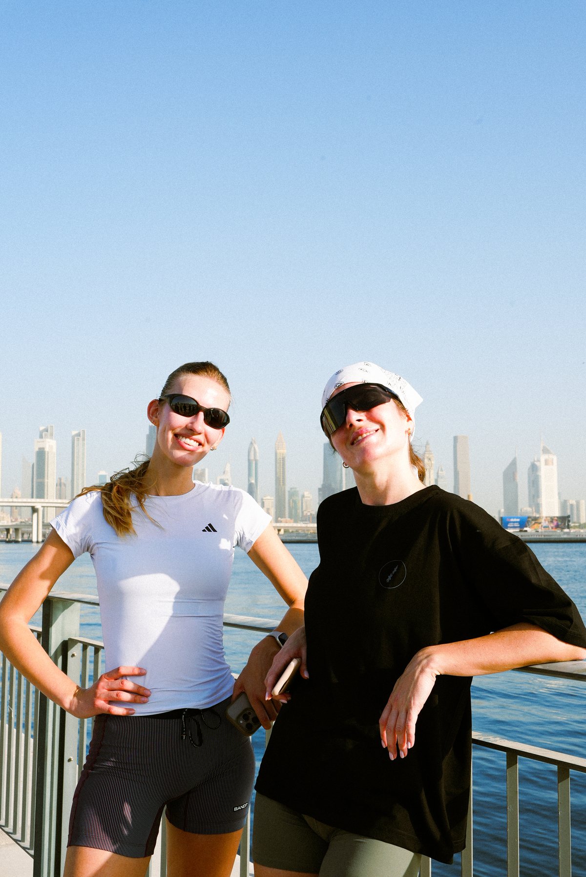 Two runners in sunglasses smiling by the water after the Saturday long run, the Dubai skyline behind